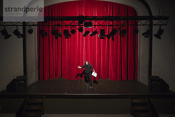Probender Schauspieler mit Drehbuch steht auf der Theaterbühne vor rotem Vorhang