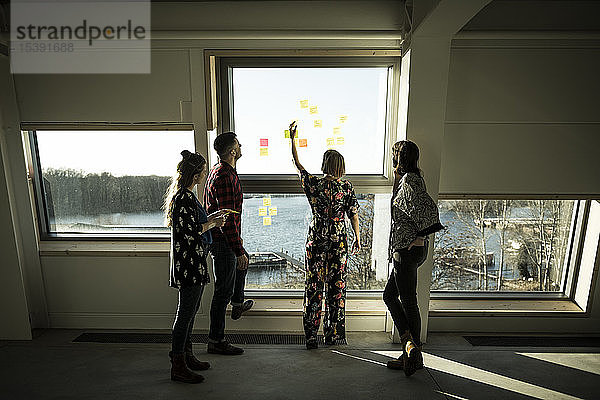 Kreatives professionelles Stehen im Büro  Brainstorming  Haftnotizen an ein Fenster kleben