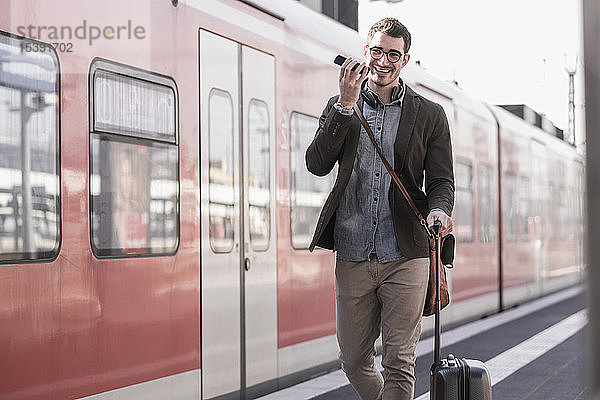 Glücklicher junger Mann mit Handy auf Bahnsteig entlang des S-Bahnsteigs
