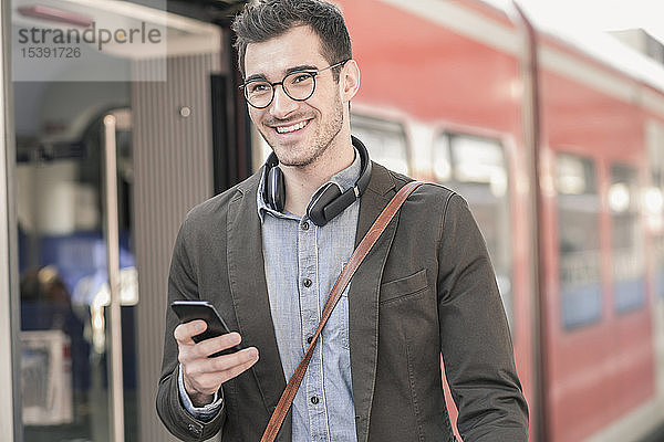 Lächelnder junger Mann mit Handy im Nahverkehrszug