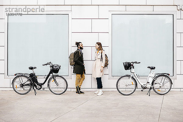 Mann und Frau mit E-Fahrrädern stehen vor einem Gebäude und unterhalten