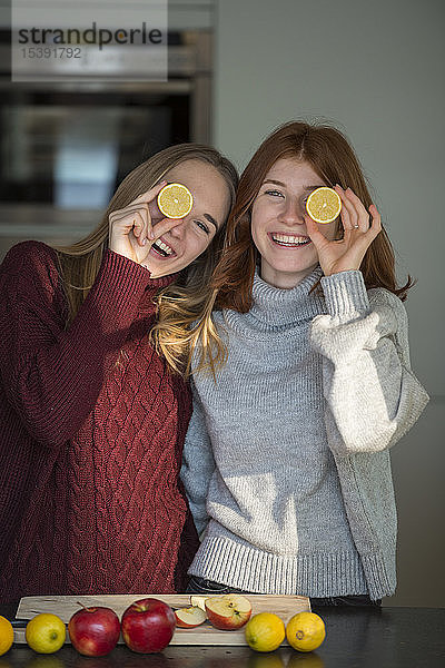 Zwei lachende Freunde halten sich Zitronenhälften vor die Augen