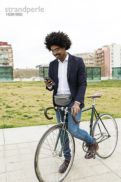 Spanien  Barcelona  lächelnder Geschäftsmann auf dem Fahrrad mit Handy in der Stadt