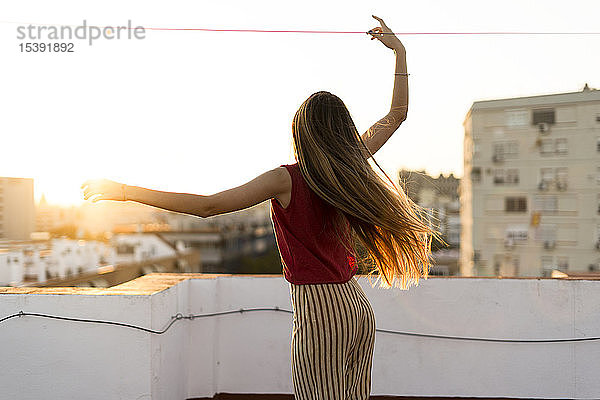 Rückansicht eines anmutigen Teenager-Mädchens  das sich bei Sonnenuntergang auf der Dachterrasse der Stadt bewegt