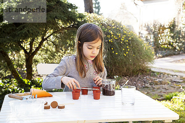 Porträt eines kleinen Mädchens am Gartentisch beim Säen von Samen