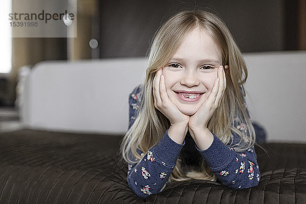 Porträt eines lächelnden kleinen Mädchens mit Zahnlücke und Kopf in den Händen