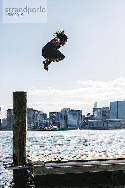 USA  New York  Brooklyn  junger Mann beim Parkour-Sprung vom Holzpfahl vor der Skyline von Manhattan