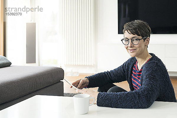 Porträt einer lächelnden Frau mit digitalem Tablett  die zu Hause auf dem Boden sitzt