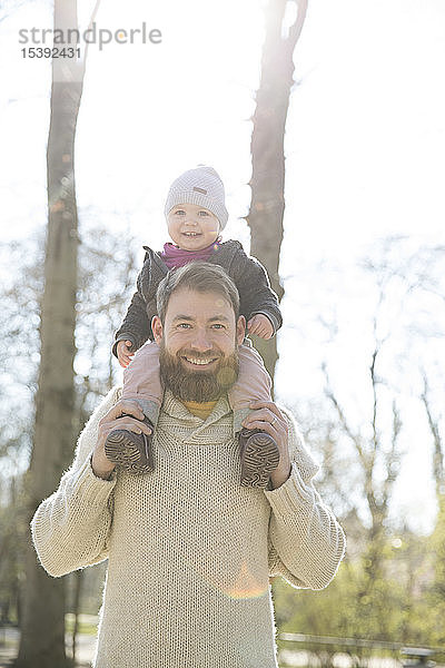 Porträt eines glücklichen Vaters  der seine Tochter im Park auf den Schultern trägt