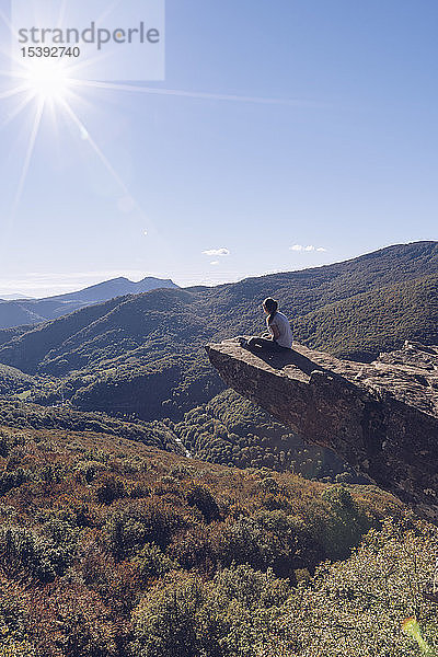 Spanien  Navarra  Wald von Irati  Frau sitzt auf einem Felssporn über einer Waldlandschaft im Gegenlicht