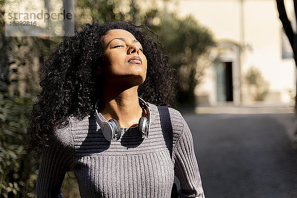 Porträt einer Frau mit Kopfhörern  die mit geschlossenen Augen die Sonne genießt