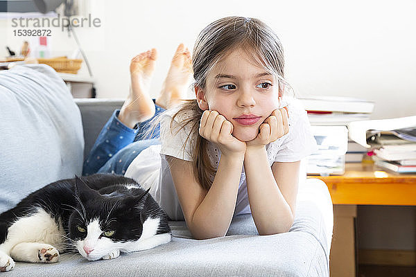 Porträt eines kleinen auf dem Sofa liegenden Mädchens mit Katze