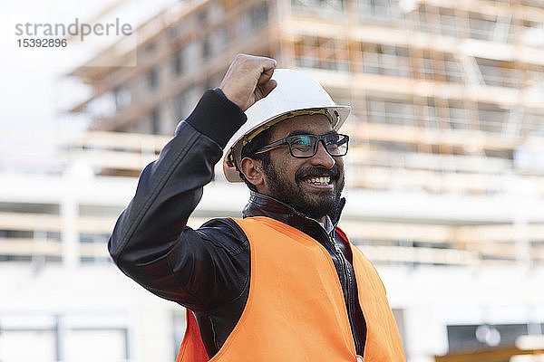 Porträt eines glücklichen Bauingenieurs vor der Baustelle mit Schutzhelm und Sicherheitsweste