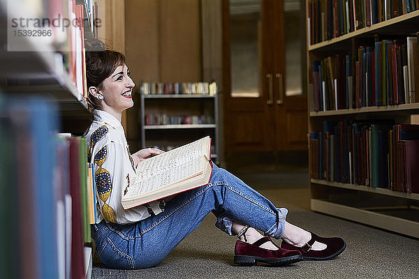 Studentin liest Buch in einer öffentlichen Bibliothek