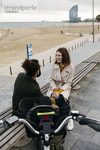 Ehepaar sitzt auf einer Bank an der Strandpromenade neben dem E-Bike und unterhält sich