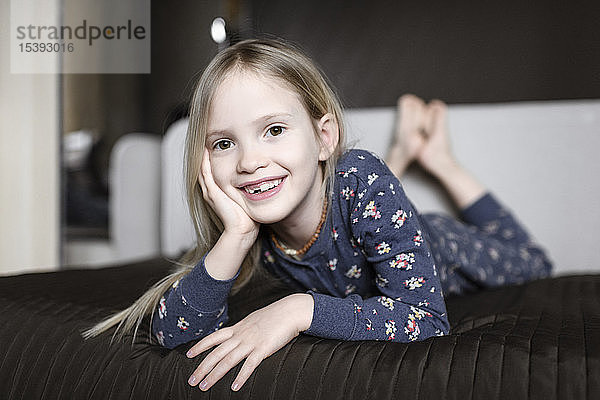 Porträt eines lächelnden kleinen Mädchens mit Zahnlücke  das sich zu Hause auf der Couch entspannt