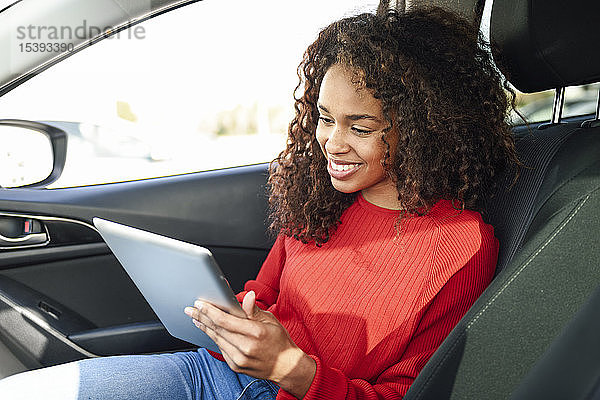 Lächelnde junge Frau mit Tablette im Auto