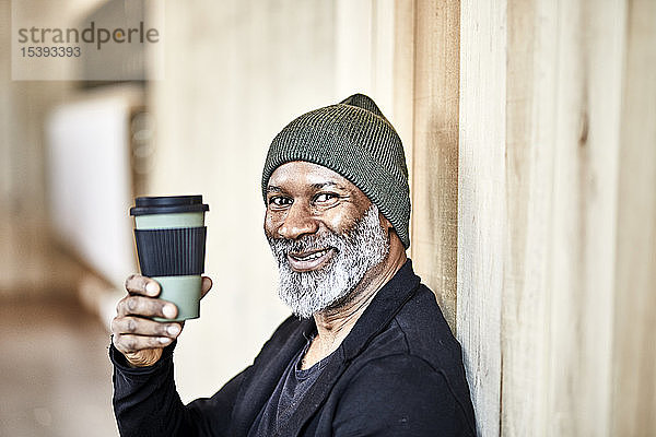 Porträt eines glücklichen reifen Geschäftsmannes mit Kaffee zum Mitnehmen an der Holzwand