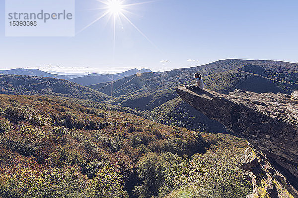 Spanien  Navarra  Wald von Irati  Frau sitzt auf einem Felssporn über einer Waldlandschaft im Gegenlicht