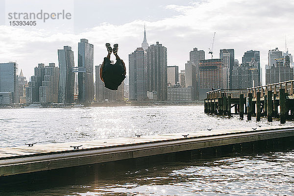 USA  New York  Brooklyn  junge Männer beim Rückwärtssalto auf dem Pier vor der Skyline von Manhattan