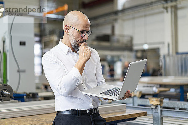 Fokussierter Geschäftsmann benutzt Laptop in Fabrik