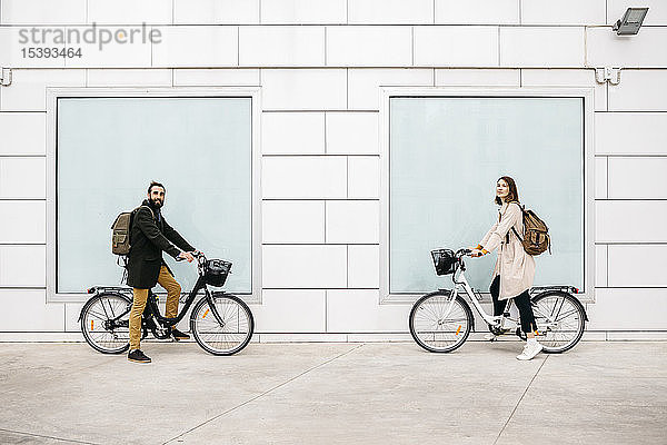 Porträt eines Mannes und einer Frau mit E-Fahrrädern an einem Gebäude stehend