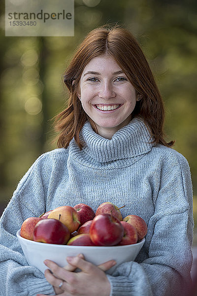 Porträt eines glücklichen rothaarigen Teenagers  der eine Schale mit Äpfeln hält