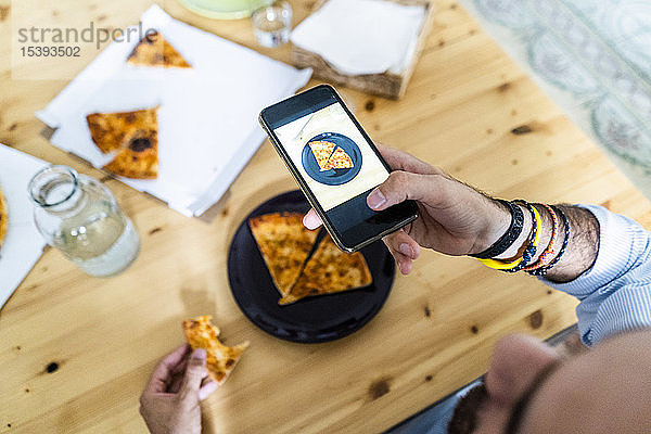 Person  die ein Smartphone-Foto von einem Stück Pizza auf einem Teller macht