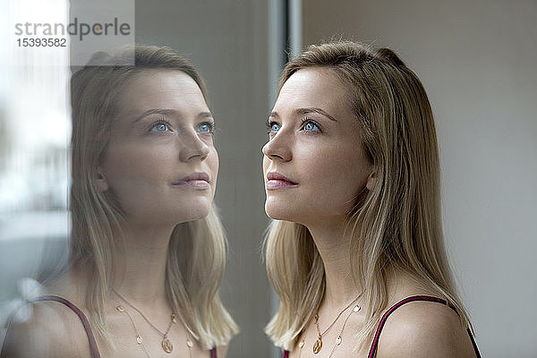 Porträt einer blonden jungen Frau und ihre Reflexion auf einer Fensterscheibe
