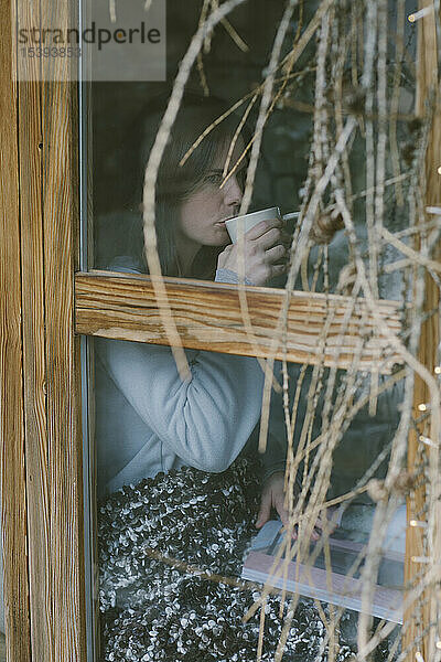 Frau hinter dem Fenster beim Teetrinken