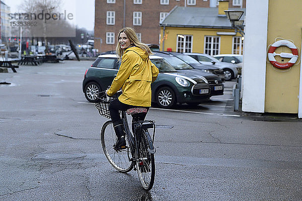 Dänemark  Kopenhagen  glückliche Frau fährt bei Regenwetter Fahrrad auf der Uferpromenade