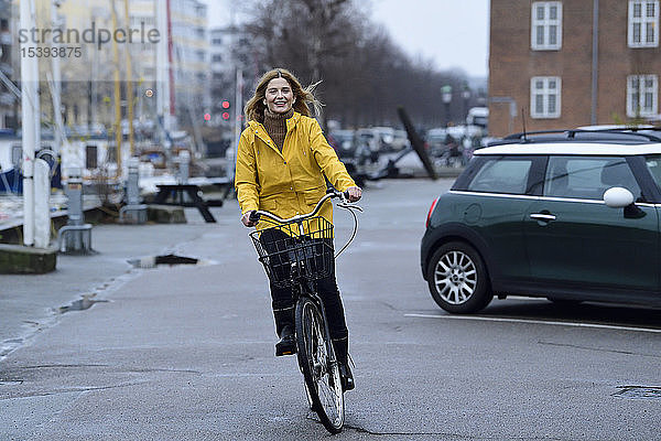 Dänemark  Kopenhagen  glückliche Frau fährt bei Regenwetter Fahrrad auf der Uferpromenade