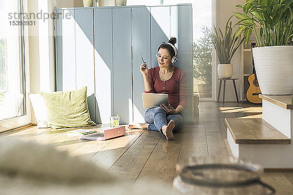 Frau mit Kopfhörern sitzt zu Hause mit Laptop am Fenster