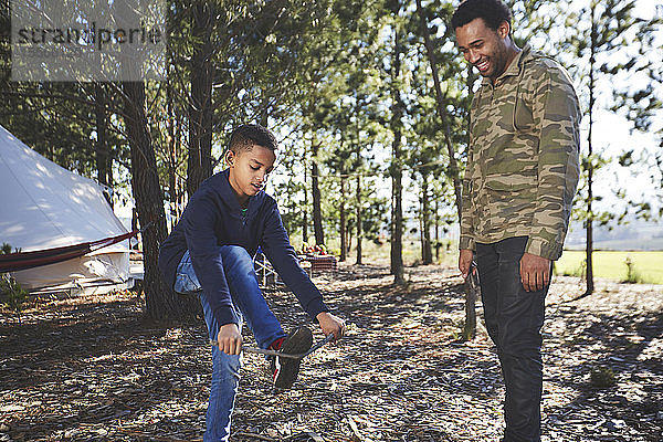 Vater beobachtet Sohn beim Zünden von Holz auf dem Campingplatz im Wald