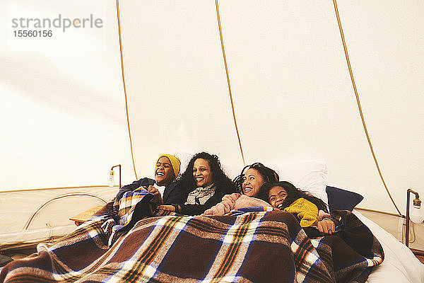 Glückliches lesbisches Paar und Kinder entspannen sich unter einer Decke im Bett in einer Camping-Jurte