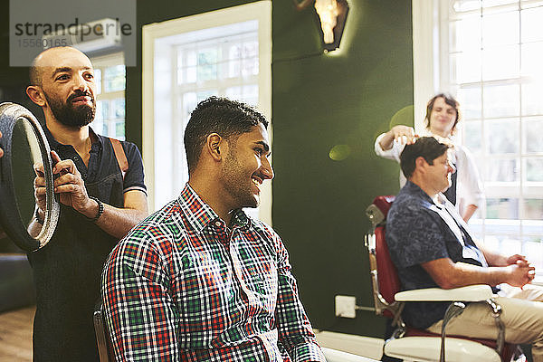 Männlicher Friseur hält Spiegel für lächelnden Kunden im Friseursalon