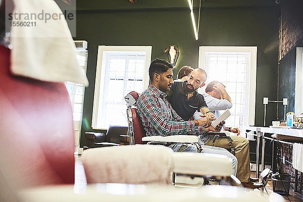 Männlicher Friseur und Kunde mit digitalem Tablet im Gespräch im Friseursalon