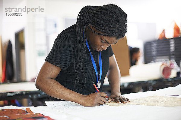 Fokussierte Modedesignerin beim Nachzeichnen eines Nähmusters im Atelier