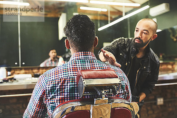 Männlicher Friseur überprüft den Haarschnitt eines Kunden in einem Friseursalon