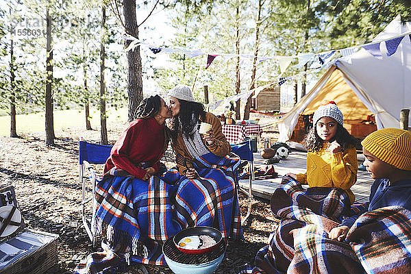 Zärtliches lesbisches Paar mit Kindern küsst sich auf einem sonnigen Campingplatz im Wald