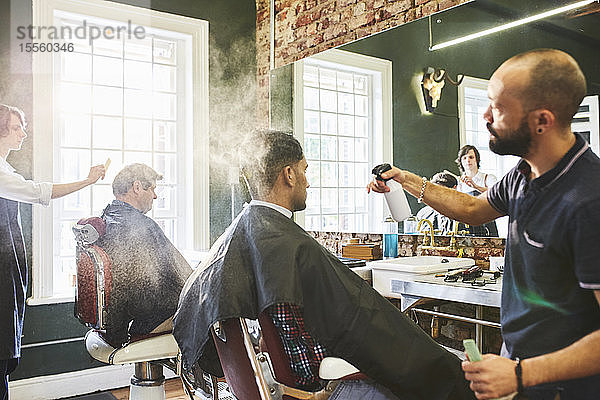 Männlicher Friseur besprüht das Haar eines Kunden im Friseursalon