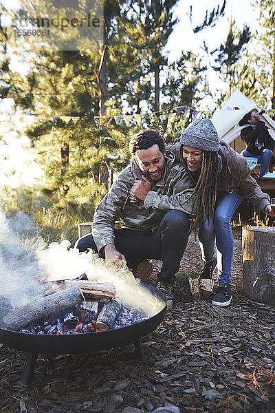 Ein glückliches Paar kümmert sich um ein Lagerfeuer auf einem Campingplatz im Wald