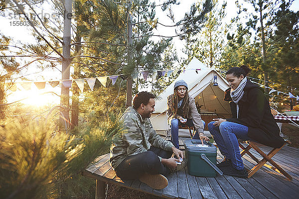 Freunde spielen Karten vor der Jurte auf einem sonnigen Campingplatz im Wald