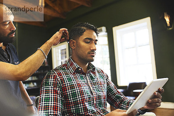 Mann benutzt digitales Tablet beim Haarschnitt im Friseursalon