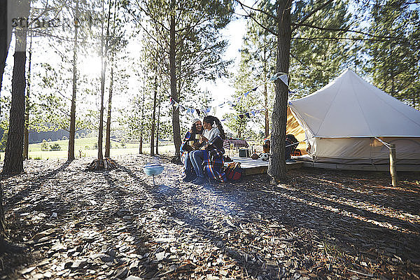 Glückliches  liebevolles lesbisches Paar entspannt sich  trinkt Kaffee auf einem sonnigen Campingplatz im Wald