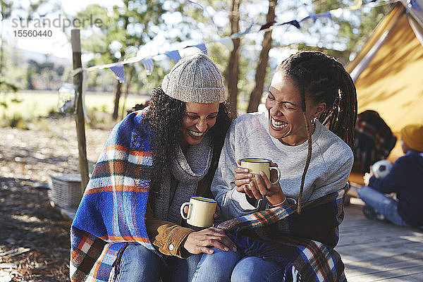 Glückliches  sorgloses lesbisches Paar  das lacht und Kaffee auf dem Campingplatz trinkt
