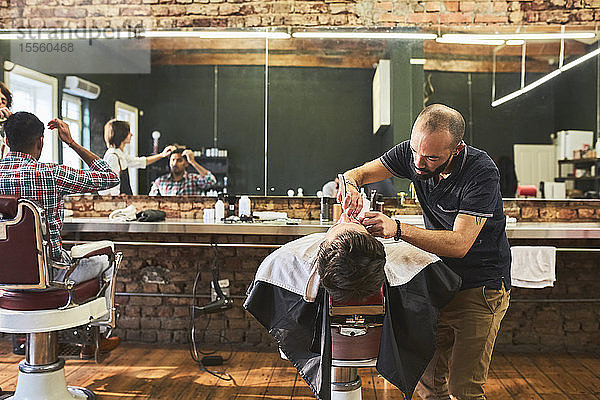 Männlicher Friseur rasiert das Gesicht eines Kunden im Friseursalon