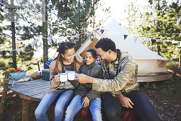 Glückliche Familie trinkt Kaffee und heiße Schokolade auf einem Campingplatz im Wald