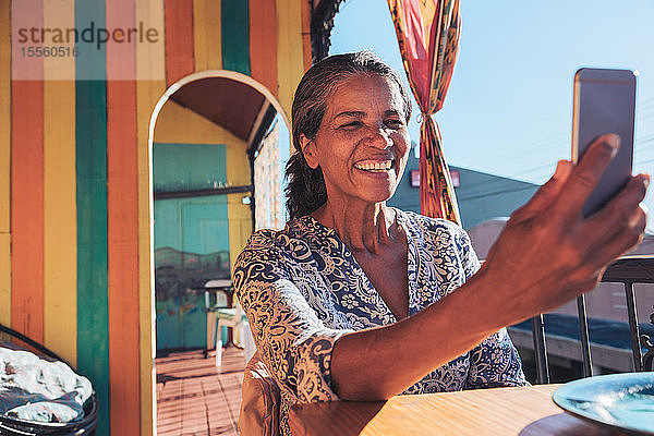 Lächelnde  glückliche Frau  die ein Selfie mit ihrem Smartphone auf einer sonnigen Terrasse macht