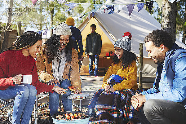 Glückliche Freunde und Familie beim Kochen am Lagerfeuer auf dem Campingplatz